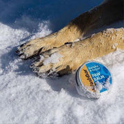 A picture of dog paws in the snow by a container of Kanuka repair paw balm made by WashBar
